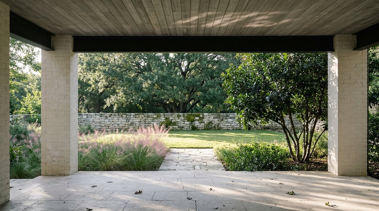 Limestone loggia opens onto a sloped garden, with a low stone wall, mountain laurel, and live oak canopy.