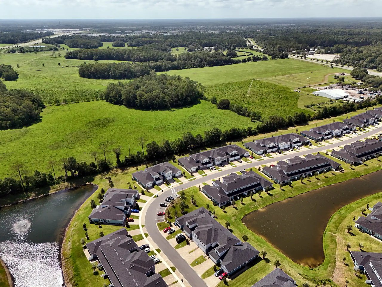 Aerial view of homes along curving streets beside ponds and a large green field.