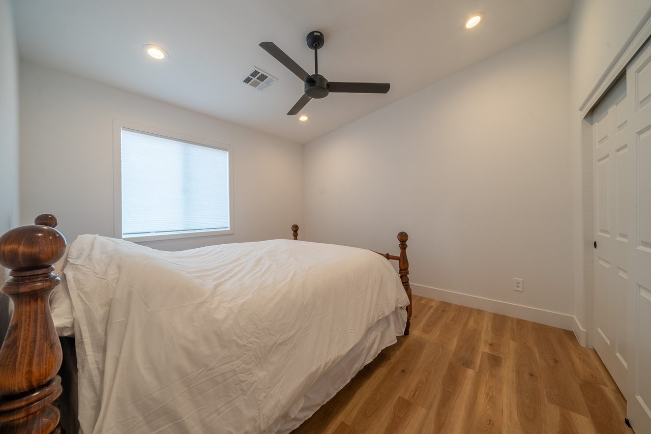 Bedroom with a wooden bed frame, white bedding, ceiling fan, and wood flooring.