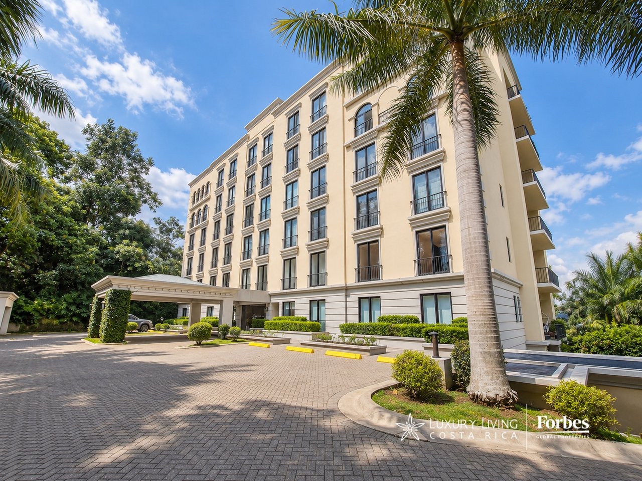 Cream-colored apartment building with balconies, palm trees, and a covered entrance.