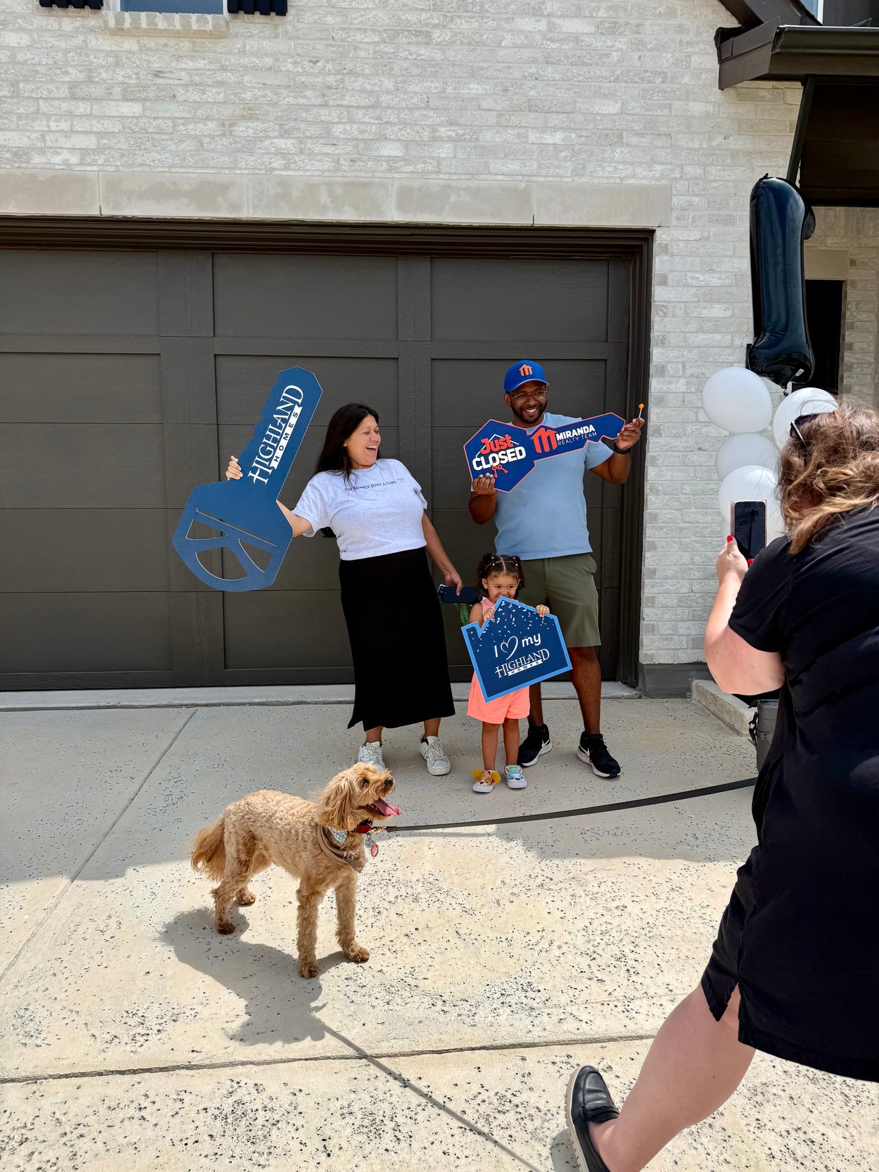 Bennett family celebrating in front of their new Highland Home at Landmark by Hillwood in Denton, Texas, holding a "Closed by Miranda Realty Team" and "Highland Homes"sign on closing day