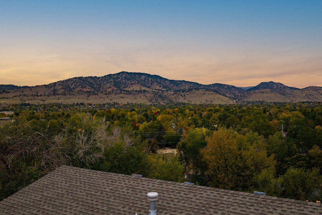 Rooftop-level view from 2003 Balsam Drive at dusk across the treetops to the foothills