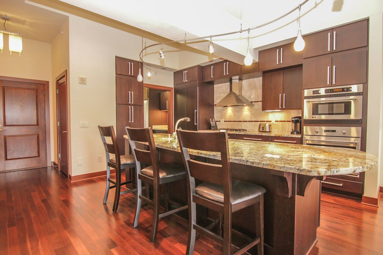 Kitchen with a large stone island, dark wood cabinets, stainless steel ovens, and hardwood floors.