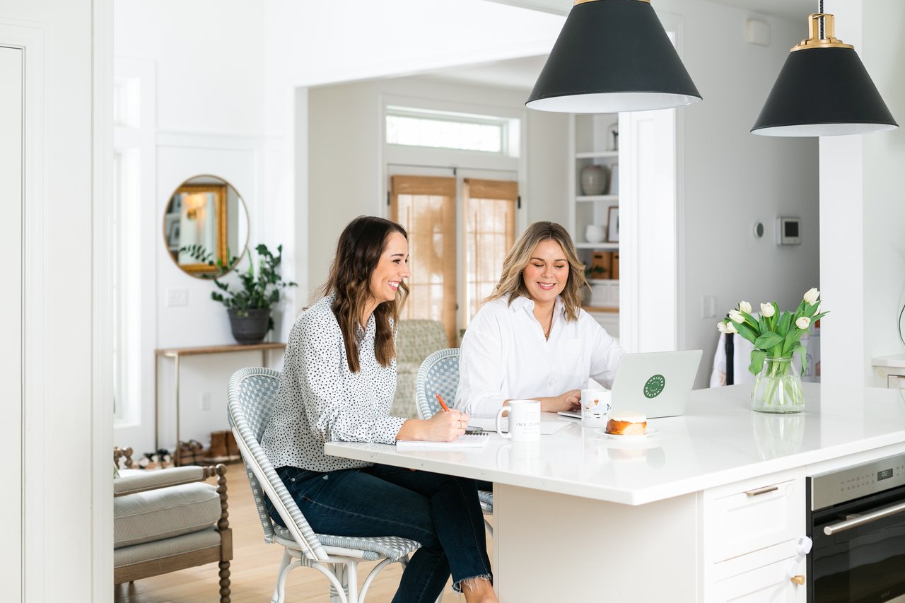 Cait Berry of Insiders Realty and a colleague strategizing at a white kitchen island, coordinating the logistics of buying and selling a home at the same time in Madison, WI.