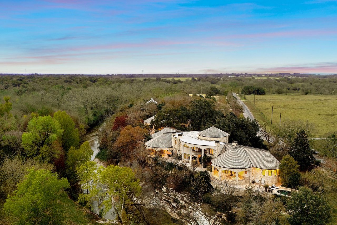 Aerial view of a stone home among trees, with a winding creek and pool.