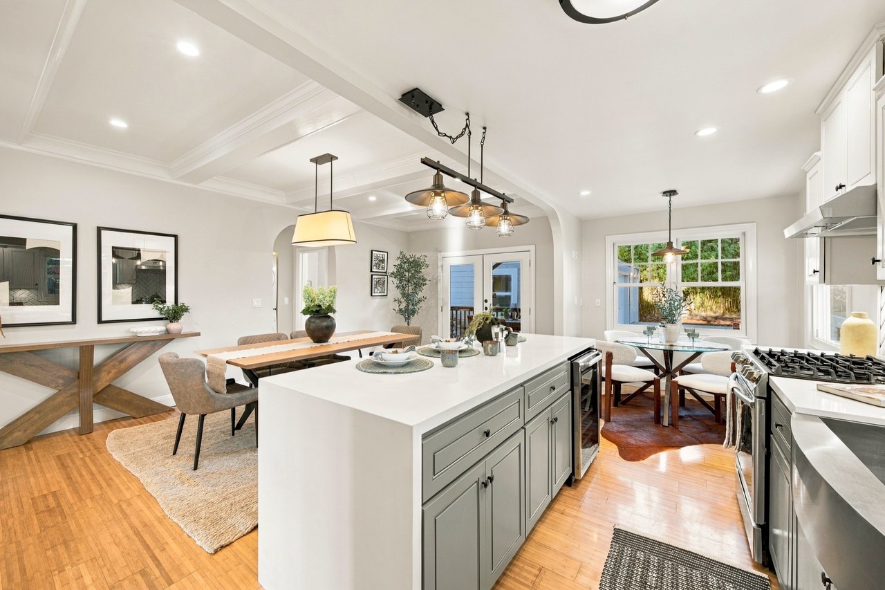 Open-plan kitchen with a large gray island, hardwood floors, and dining area beside a garden-facing window.