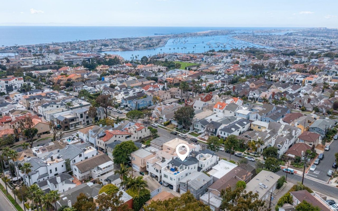  An aerial view of a coastal neighborhood in Corona del Mar, California, with a marina and the ocean in the background.