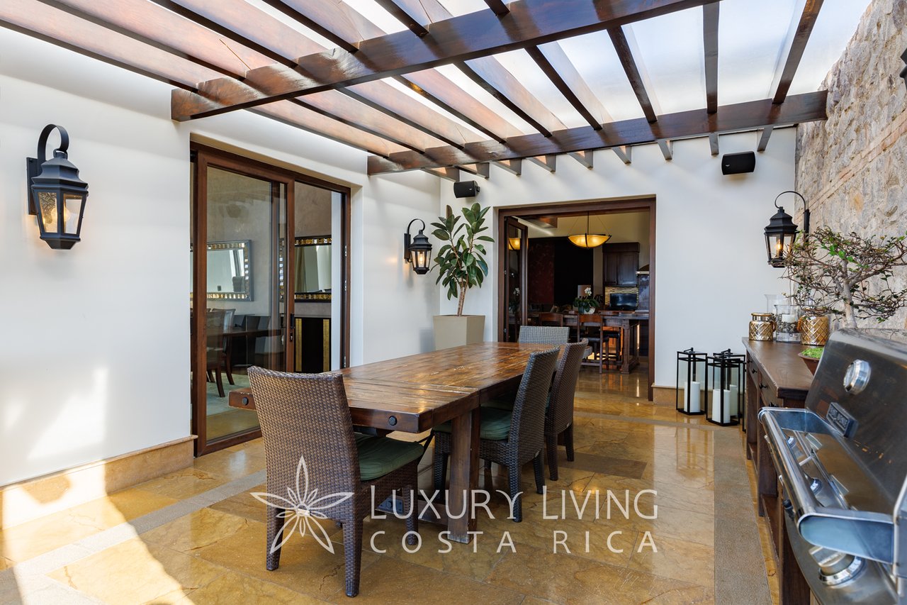 Covered dining terrace with wooden pergola, stone wall, and built-in barbecue.