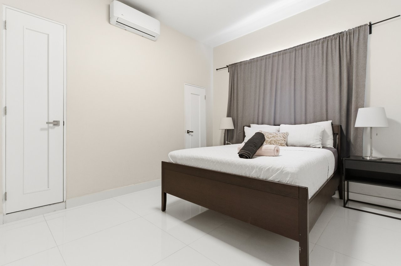 Furnished bedroom with a dark wood bed, gray curtains, and a wall-mounted air conditioner.