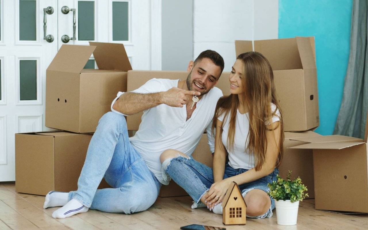 Couple sitting among moving boxes as the man holds up their new home keys.