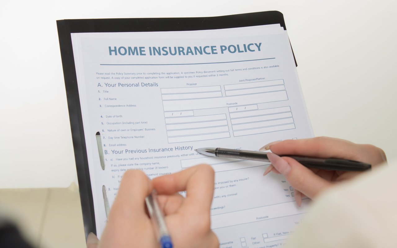 Home insurance policy form on a clipboard being filled out by hand.