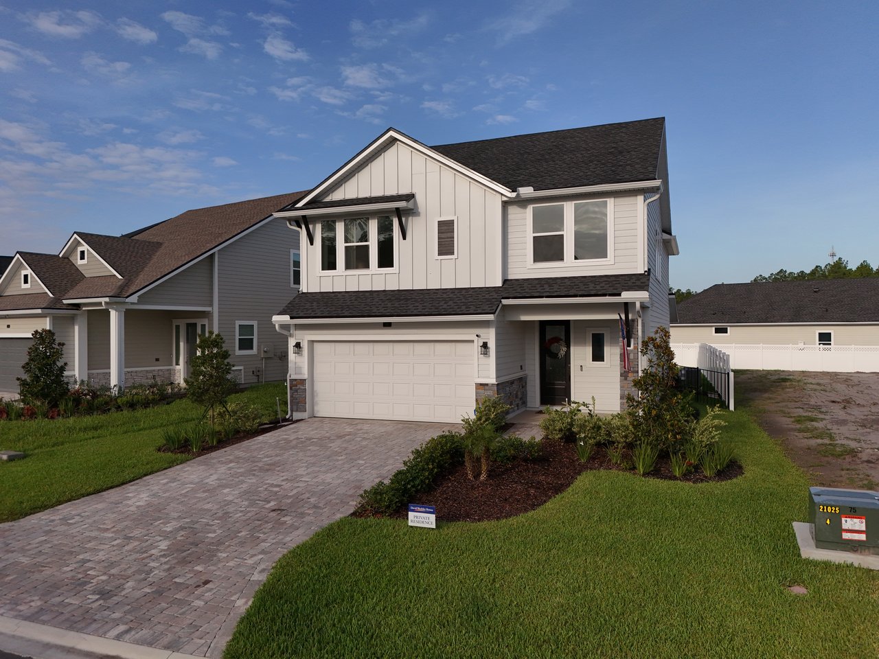 Two-story white and gray home with a double garage, paved driveway, and landscaped front yard.