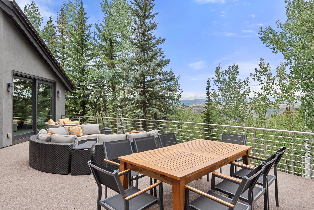 Mountain home deck with wooden dining table, lounge seating, and wooded hill views.