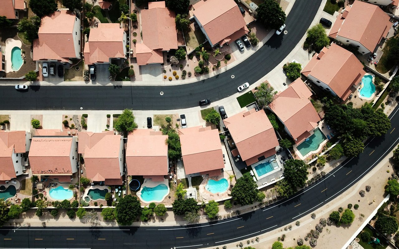 Aerial view of a subdivision with tile-roofed homes, private pools, and curving streets.