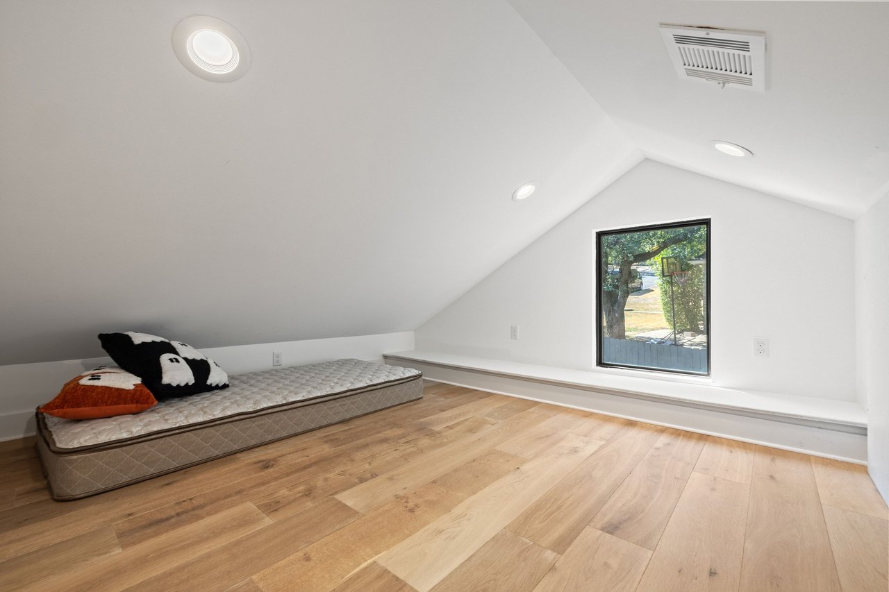Finished attic room with sloped ceiling, wood floors, and a mattress beside a window.