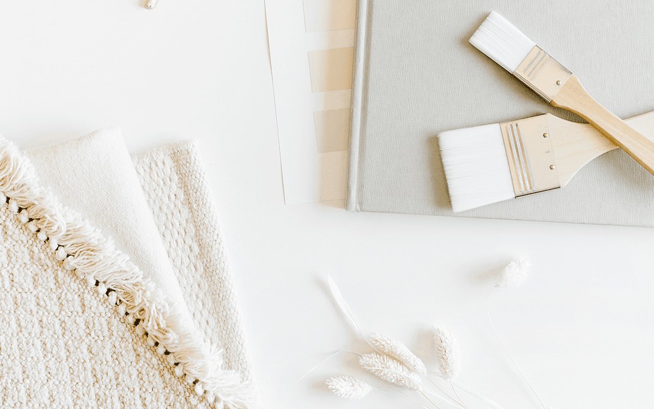 Paintbrushes and neutral paint swatches arranged with textured white fabric and dried stems.