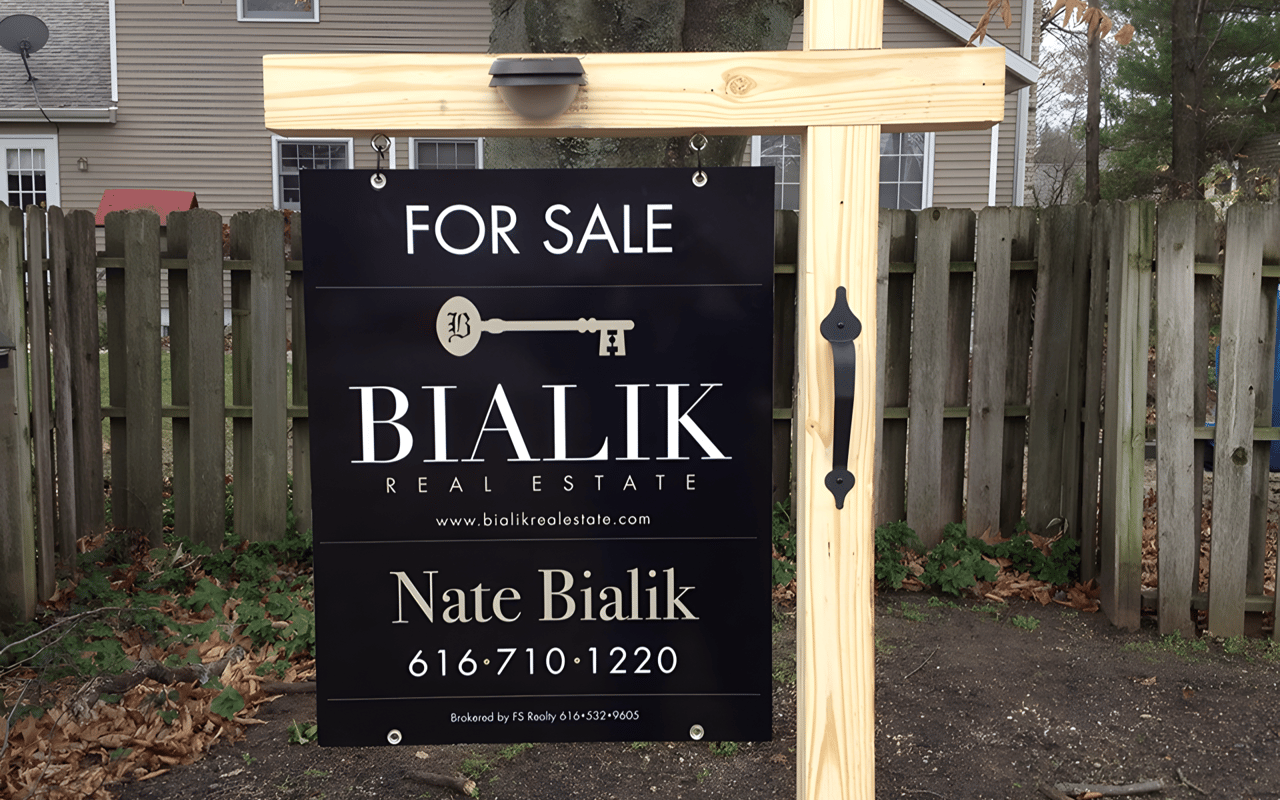 Bialik Real Estate for-sale sign with Nate Bialik’s name and phone number in front of a fence.