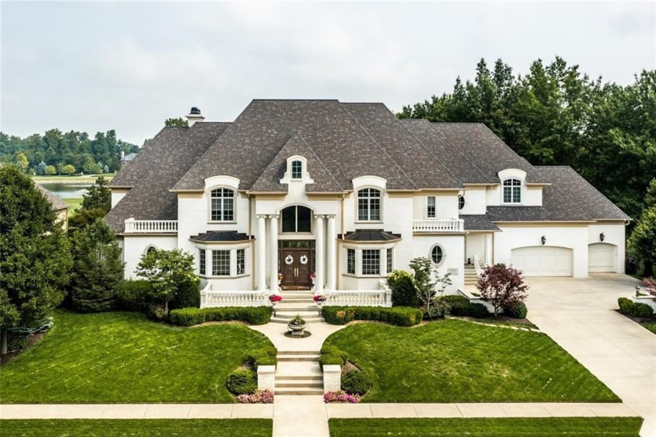 Luxury French eclectic chateau showcasing white stucco walls, symmetrical bay windows, a columned portico, a multi-car garage, and formal landscaped gardens.