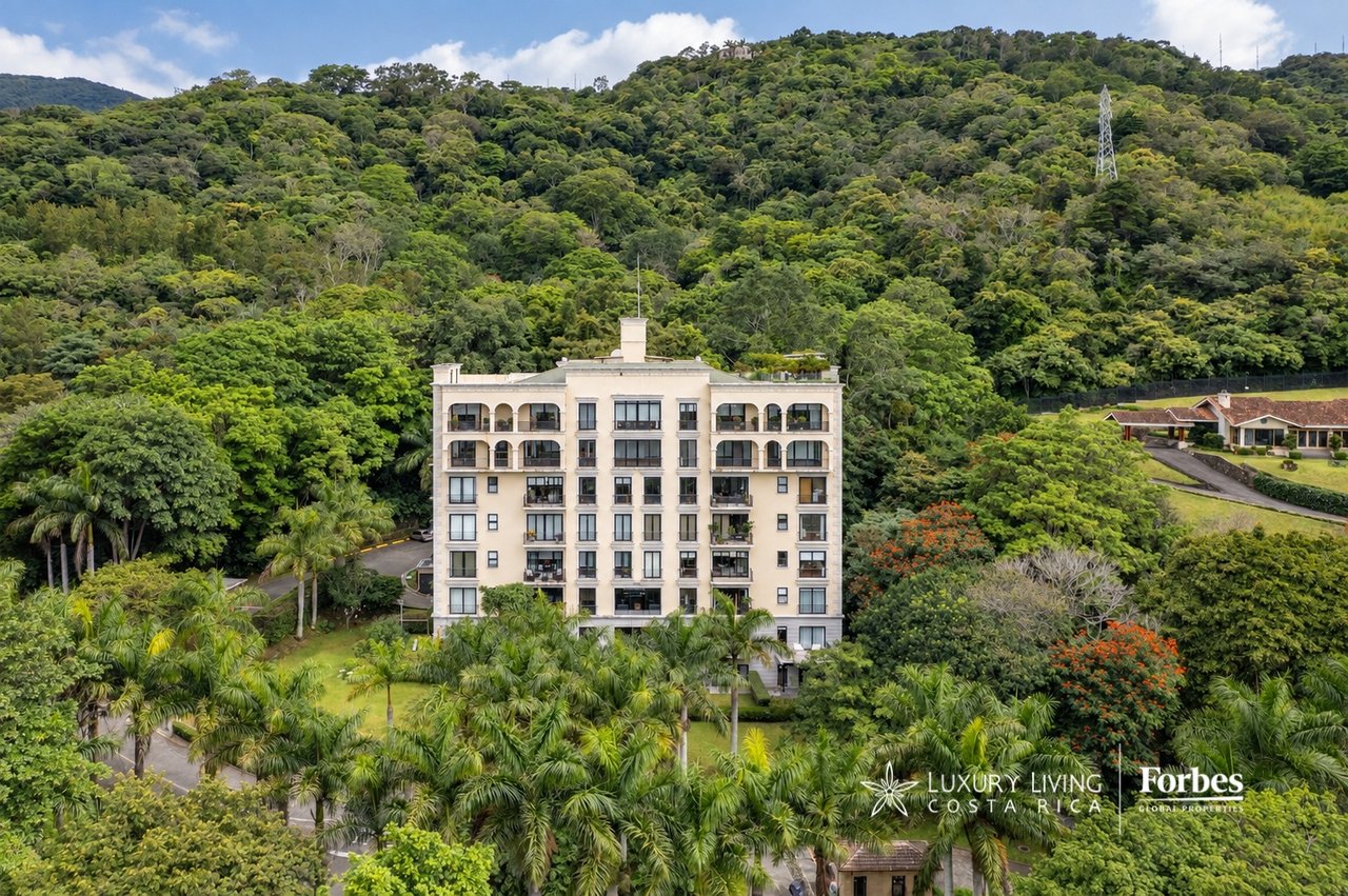 Apartment building surrounded by tropical gardens and forest on a hillside.