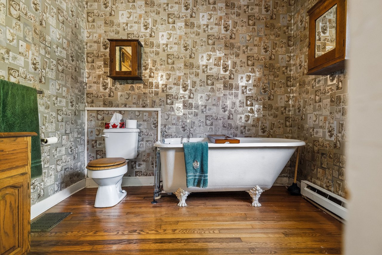 Bathroom with a white clawfoot tub, teal towel, vintage collage wallpaper, and hardwood floors.