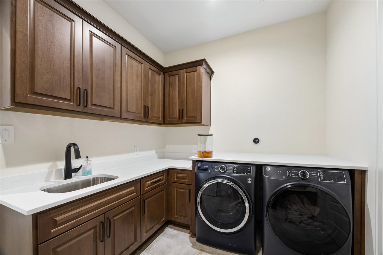 Laundry room with dark wood cabinetry, a utility sink, and front-loading washer and dryer.