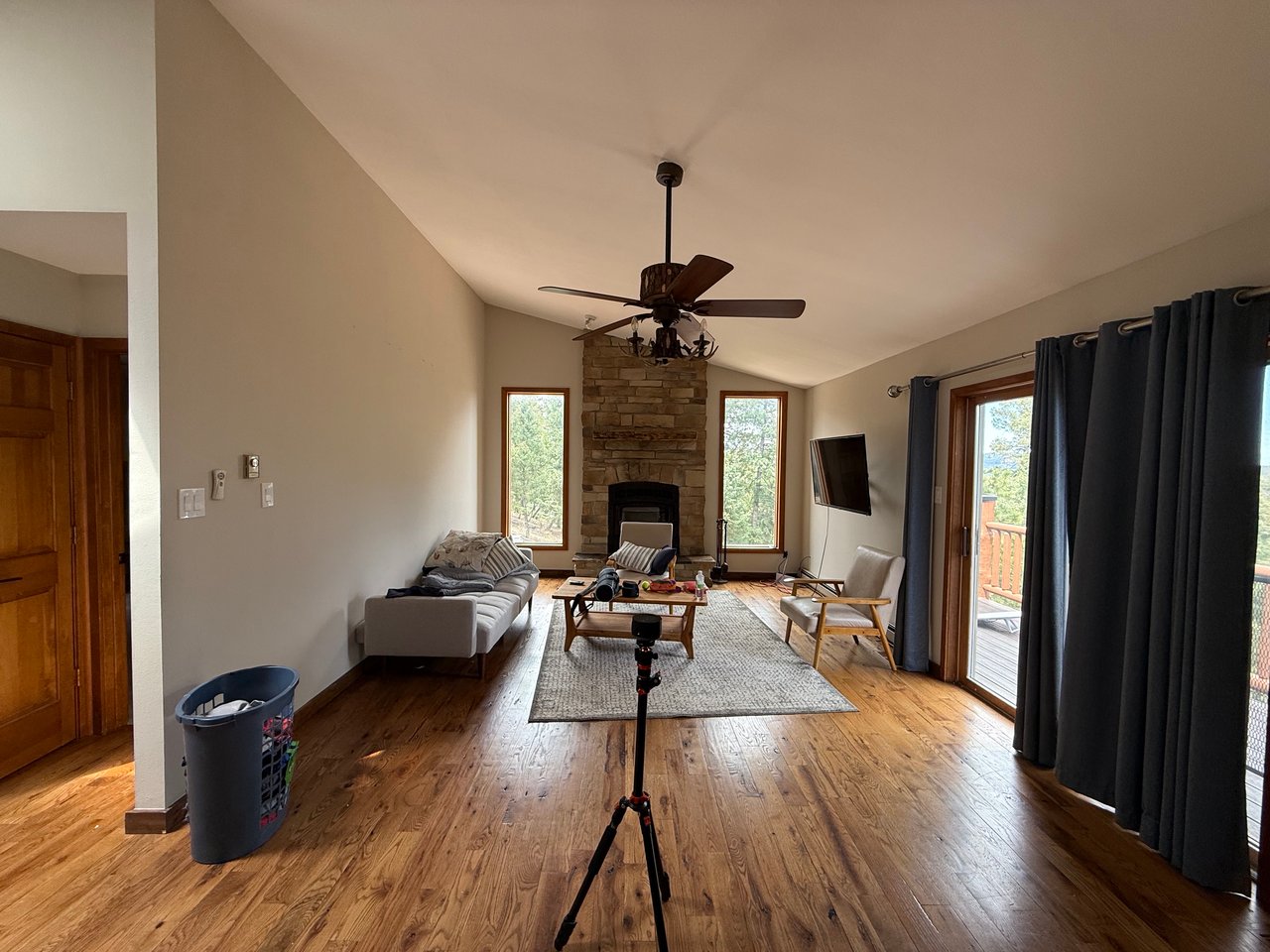 Living room with a stone fireplace, vaulted ceiling, hardwood floors, and doors opening to a deck.