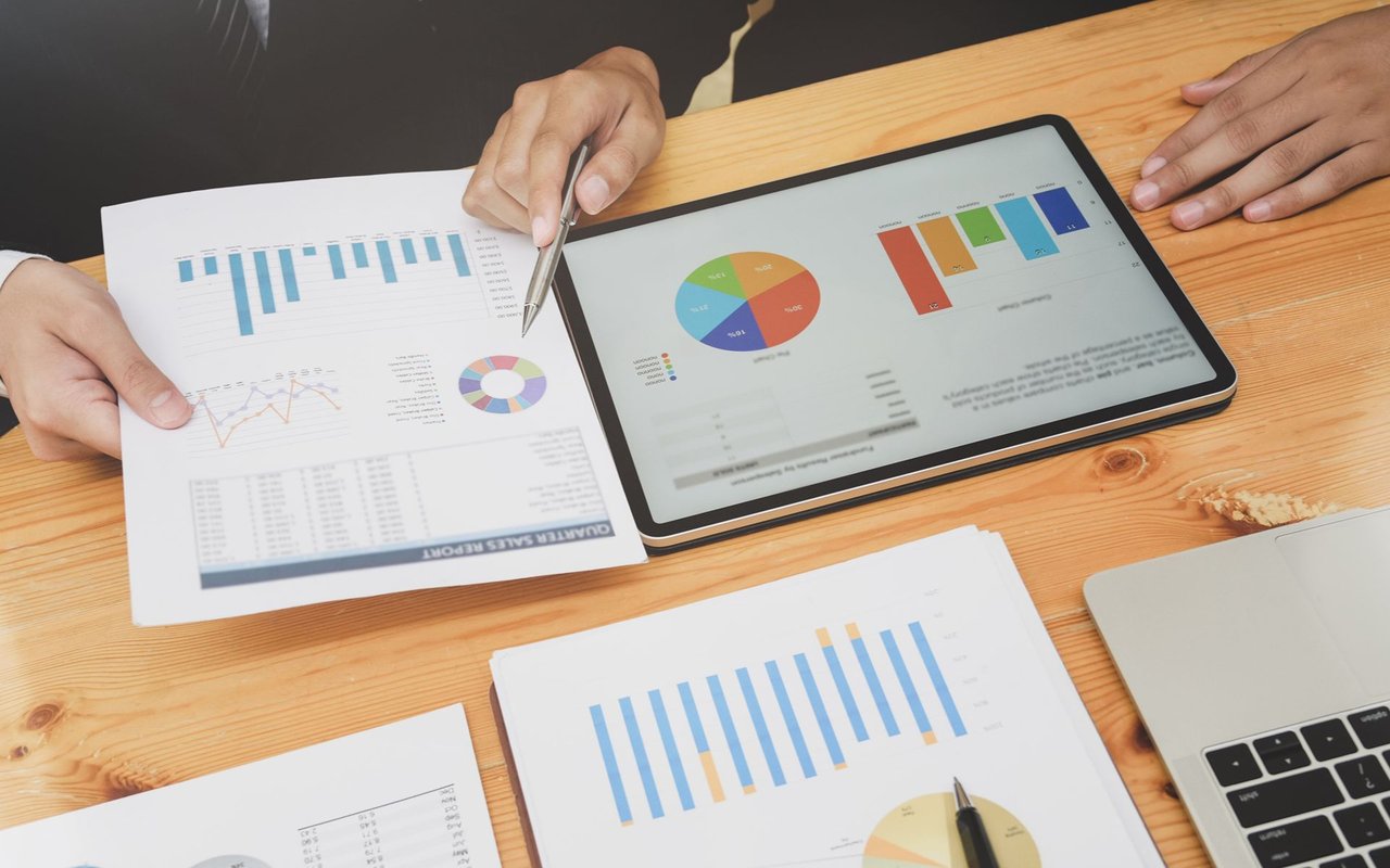 People review charts and sales reports on a tablet at a wooden table.