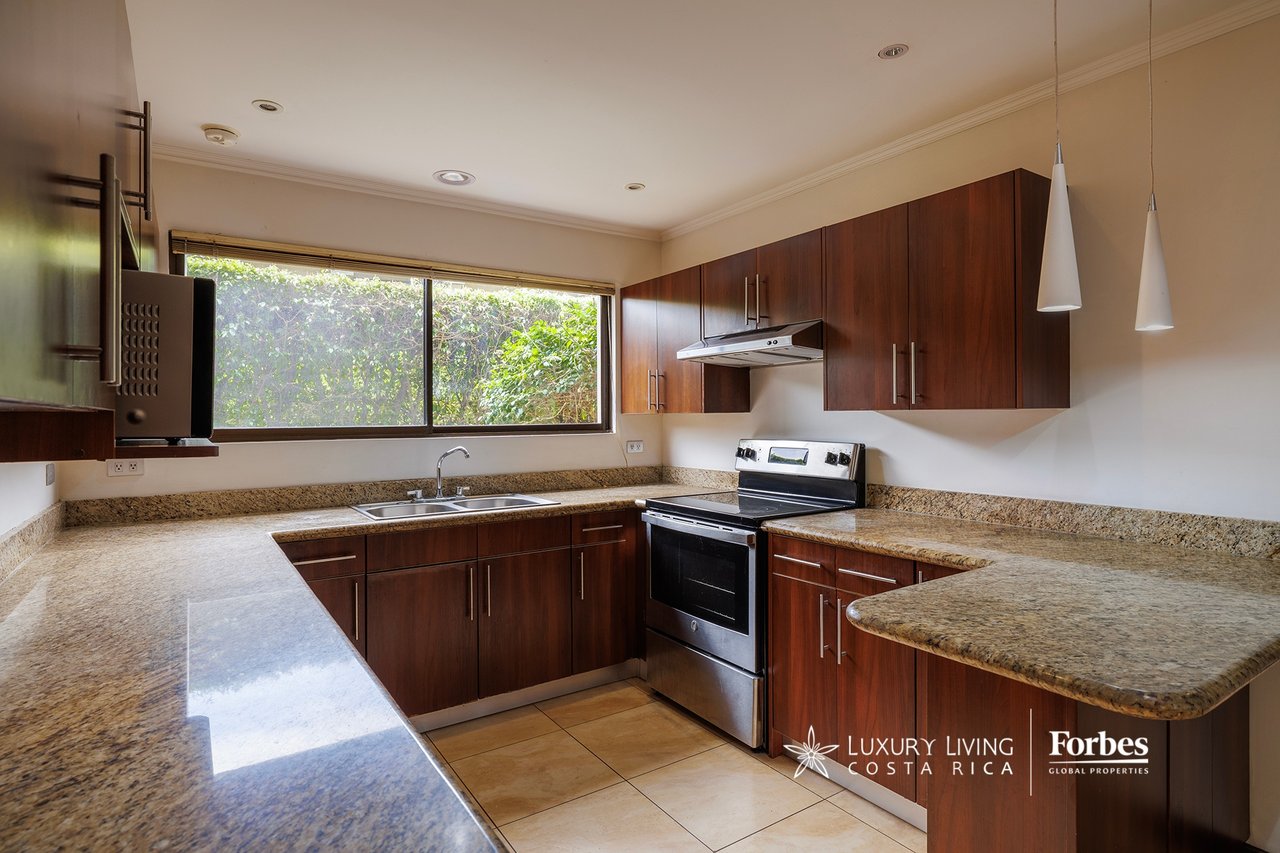 Kitchen with dark wood cabinets, granite countertops, stainless-steel range, and a wide window overlooking greenery.