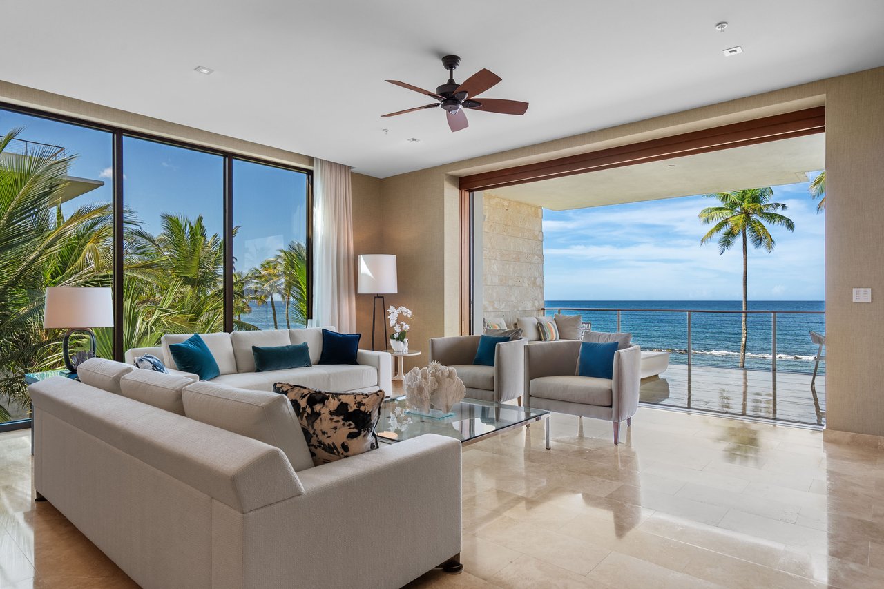 Living room with pale sofas opening onto an ocean-view terrace framed by palm trees.