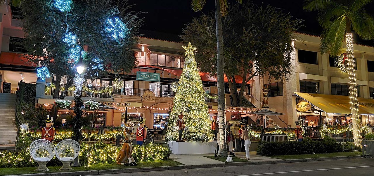 Holiday-lit shopping plaza with a glowing Christmas tree and outdoor restaurant seating.