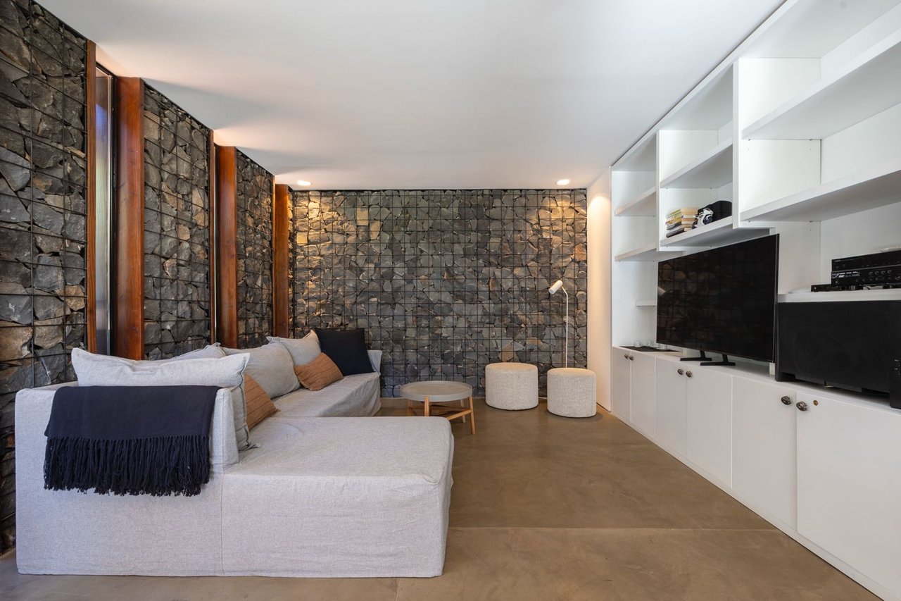 Living room with a gray sectional, rugged stone walls, and white built-in media shelving.