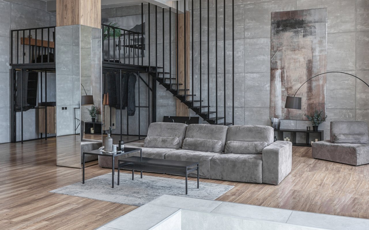 Double-height living room with a gray sectional, wood floors, and a black metal mezzanine staircase.