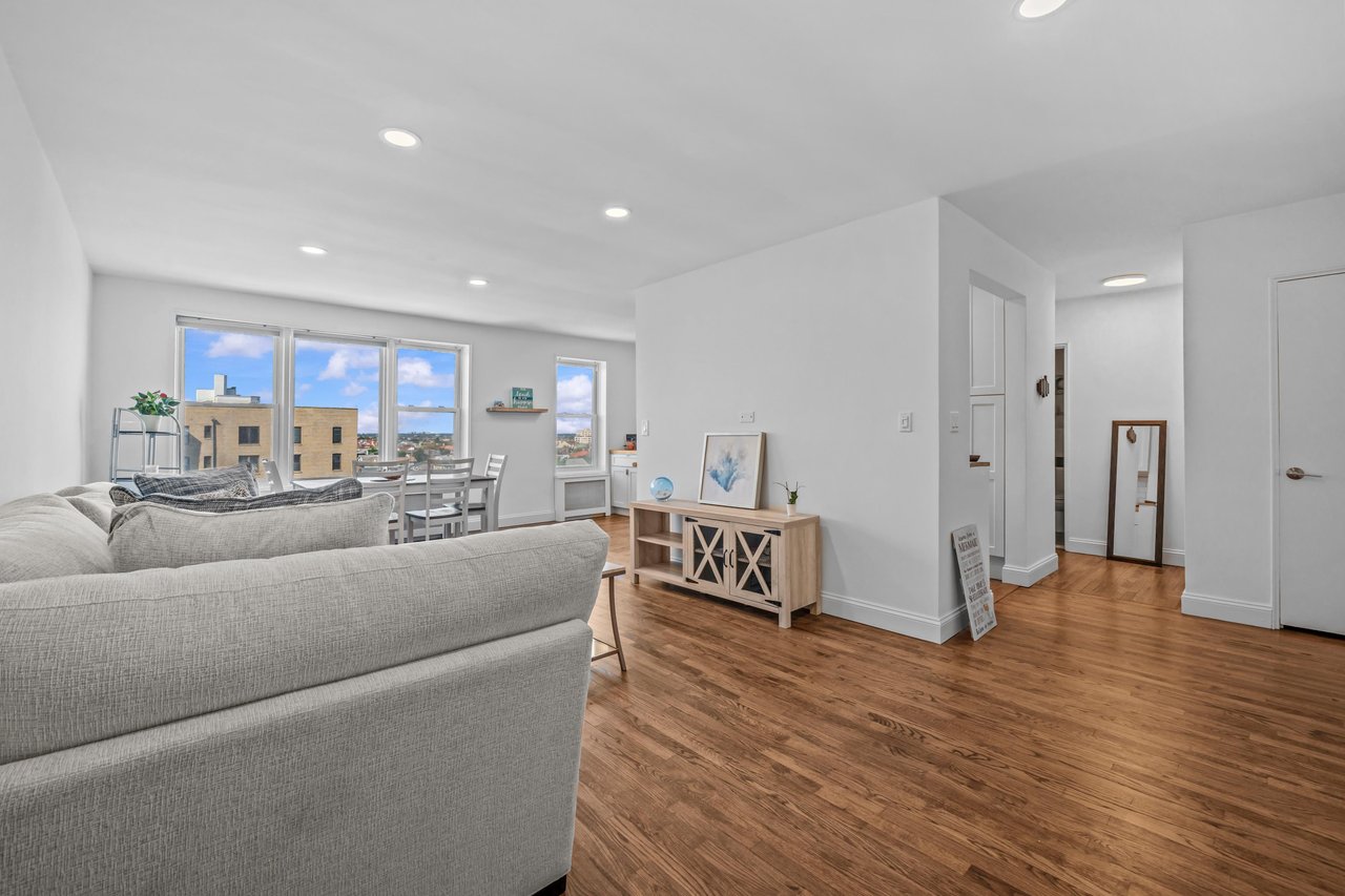 Furnished living and dining area with a gray sectional, wood floors, and large windows.
