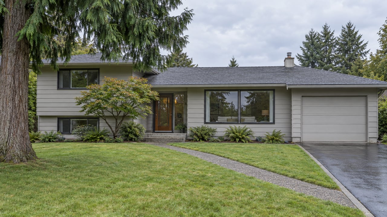 A split-level home behind a sloping lawn, with a cedar tree at left and a narrow diagonal walkway.