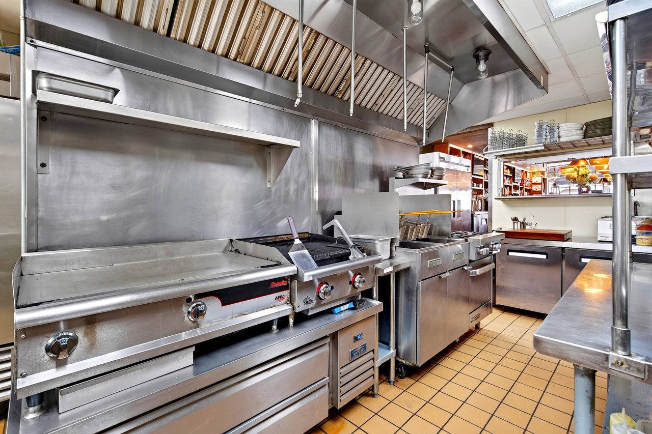 Restaurant kitchen with stainless-steel griddle and cooking equipment beneath a large ventilation hood.