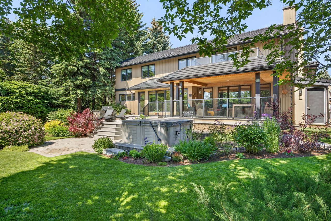 Two-story home with a covered deck and hot tub in a landscaped garden.