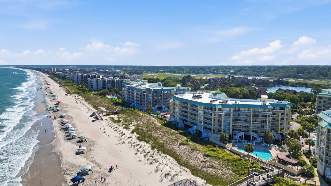Beachfront condominiums beside a sandy shore, ocean surf, and a pool.