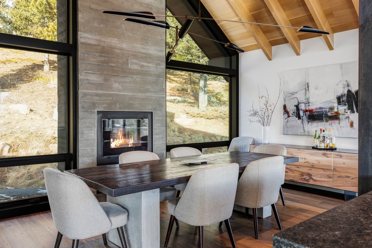 Boulder mountain home dining area with stone fireplace, upholstered chairs, and panoramic forest views