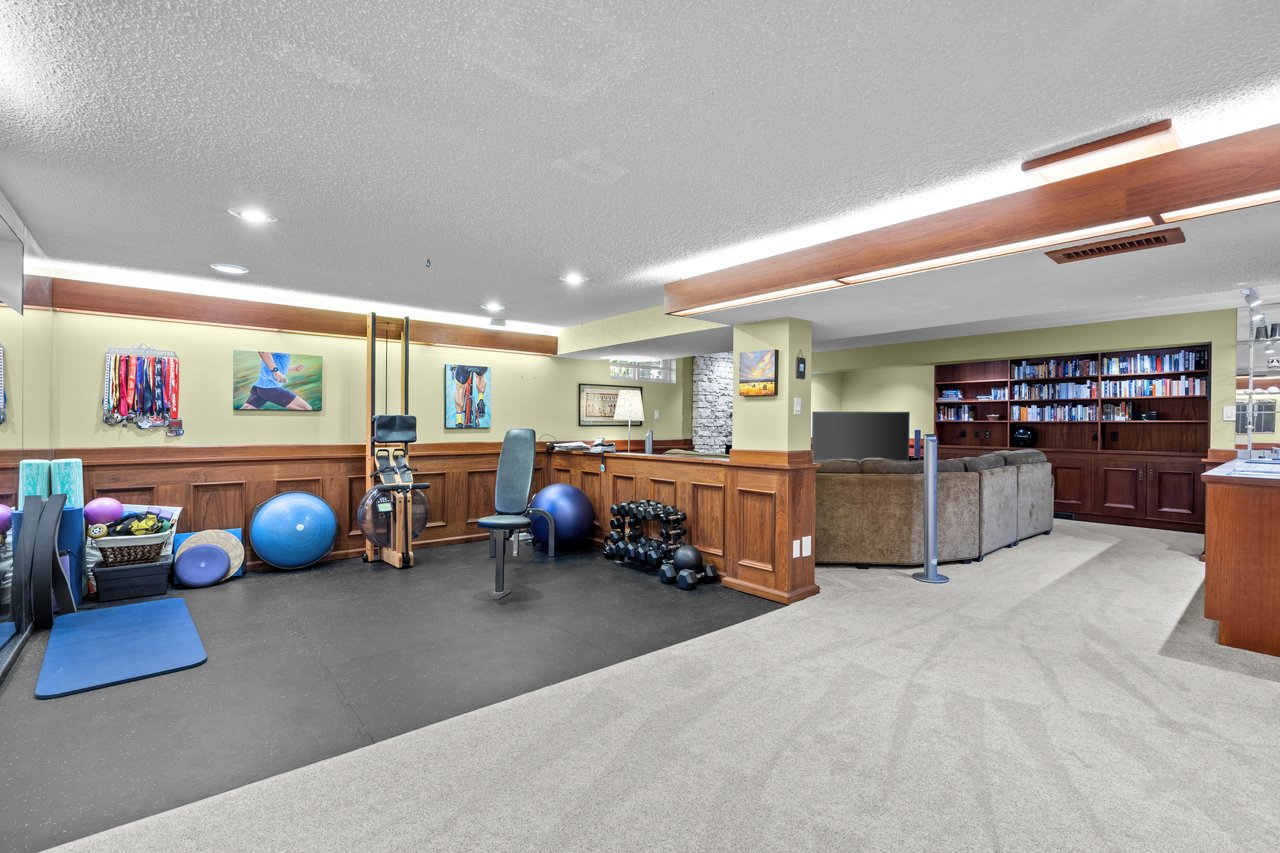 Home gym with exercise equipment and weights beside a lounge with built-in bookshelves.