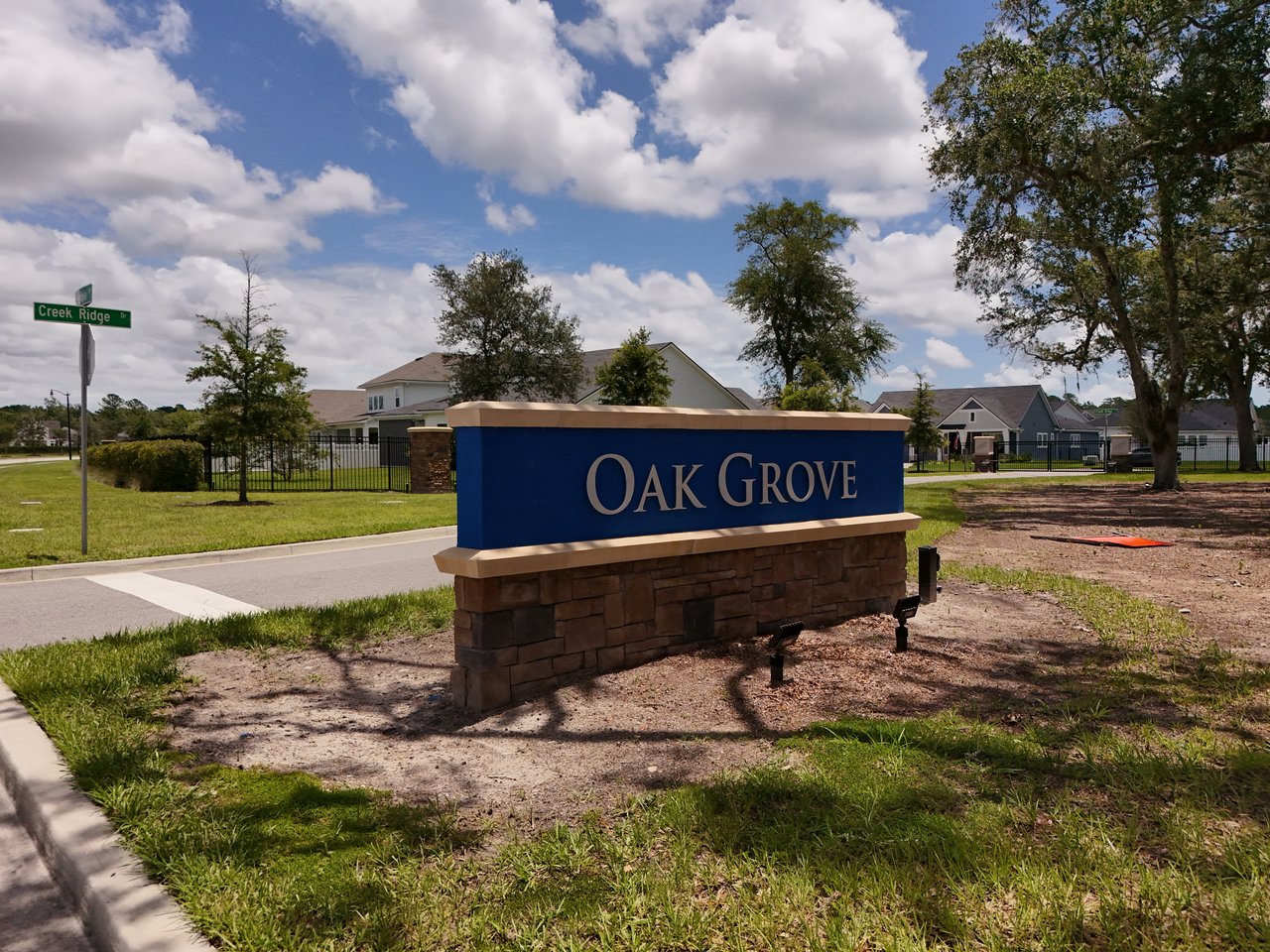 Oak Grove entrance sign beside homes on a sunny day.