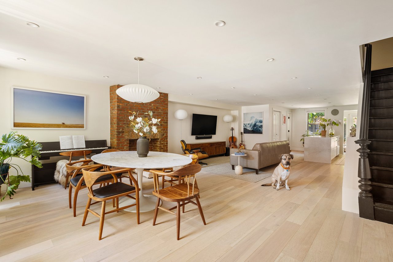 Open-plan townhouse living and dining room with exposed brick, a piano, and a seated dog.