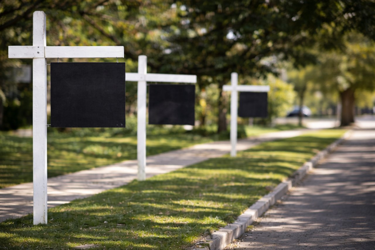 Row of empty real estate signposts along a residential sidewalk representing a slower housing market