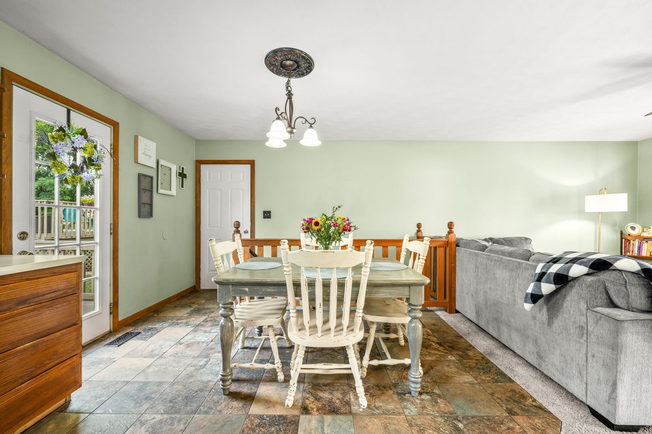 Dining area with white chairs, multicolored tile flooring, and a wood railing beside the living room.