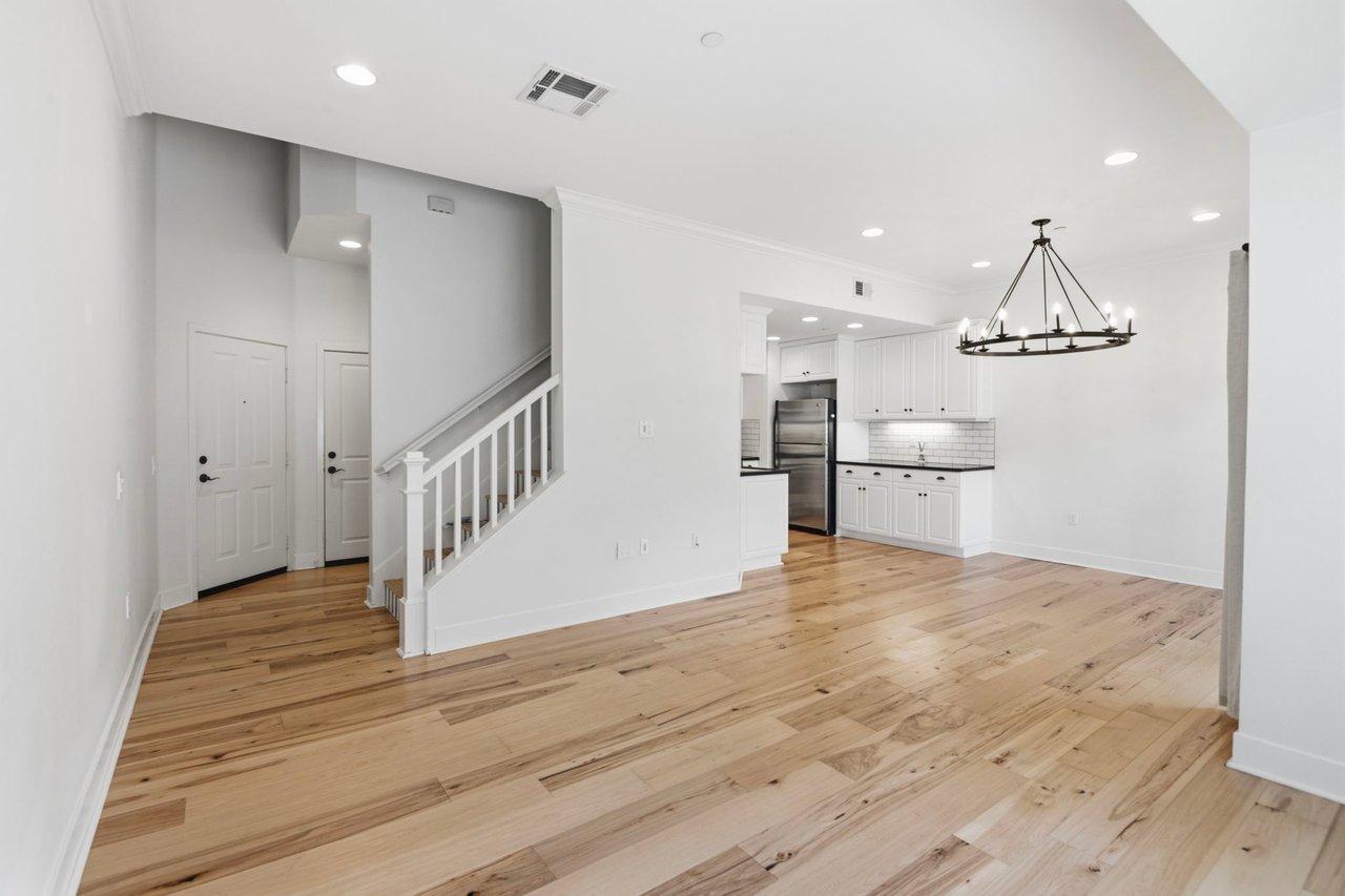 Open-concept entry and foyer with hardwood floors, white staircase railing, iron chandelier, and view into kitchen at Newport Beach townhouse