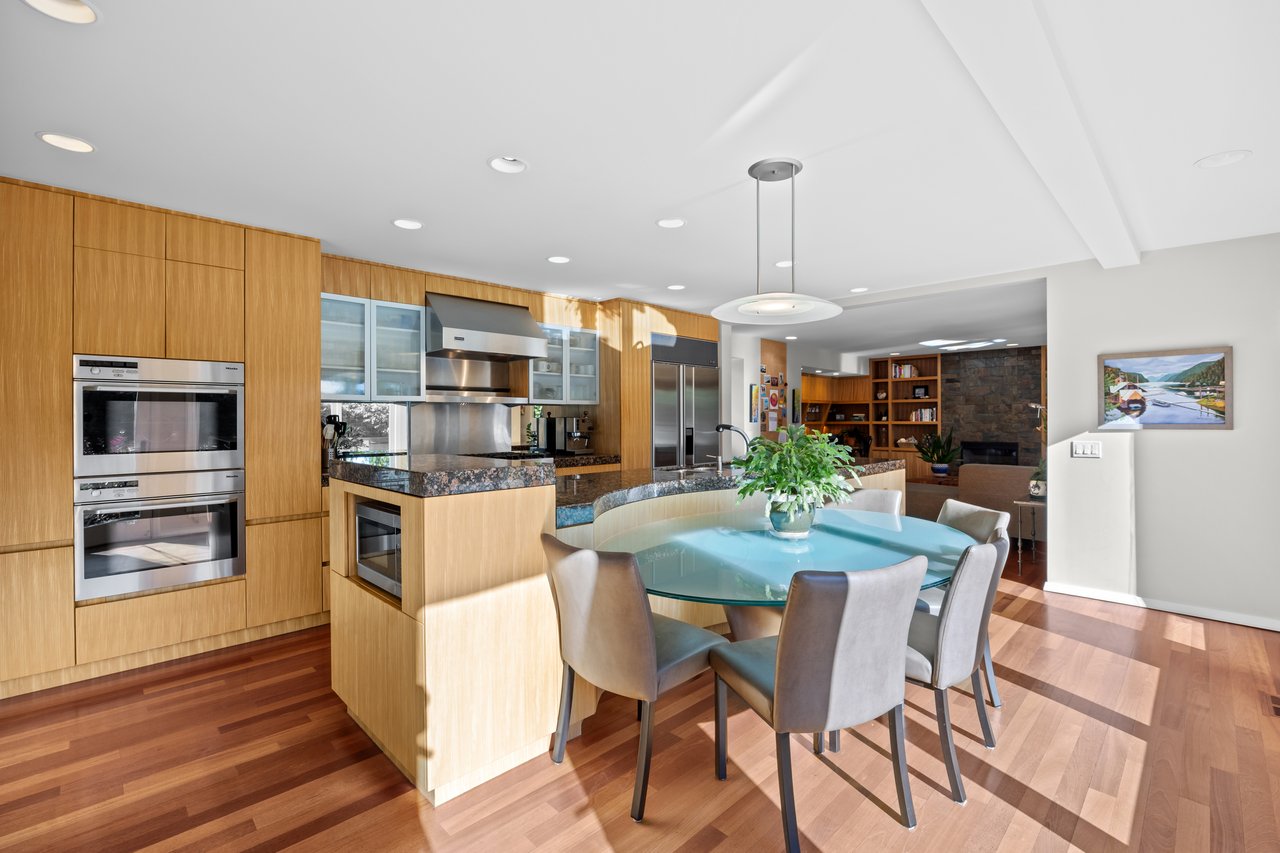 Open-plan kitchen and dining area with wood cabinetry, a granite island, and a round glass table.