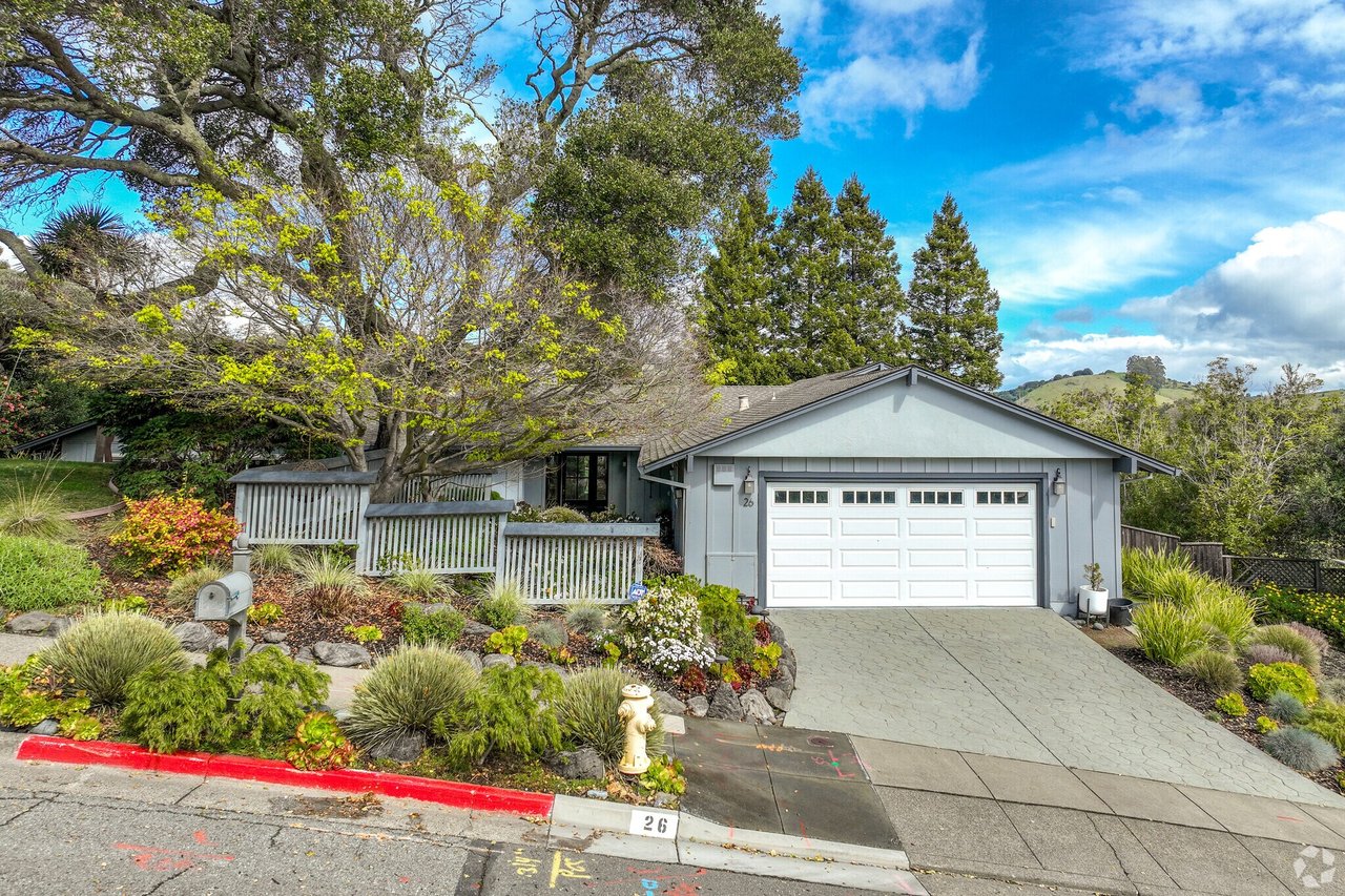 Single-story gray home with a double garage, landscaped garden, and mature trees.