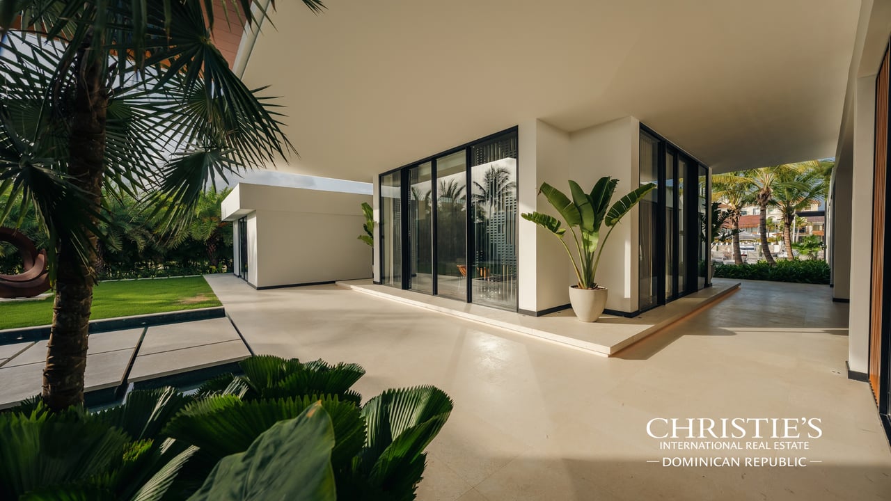 Modern villa exterior with black-framed glass walls, a covered terrace, and tropical landscaping.