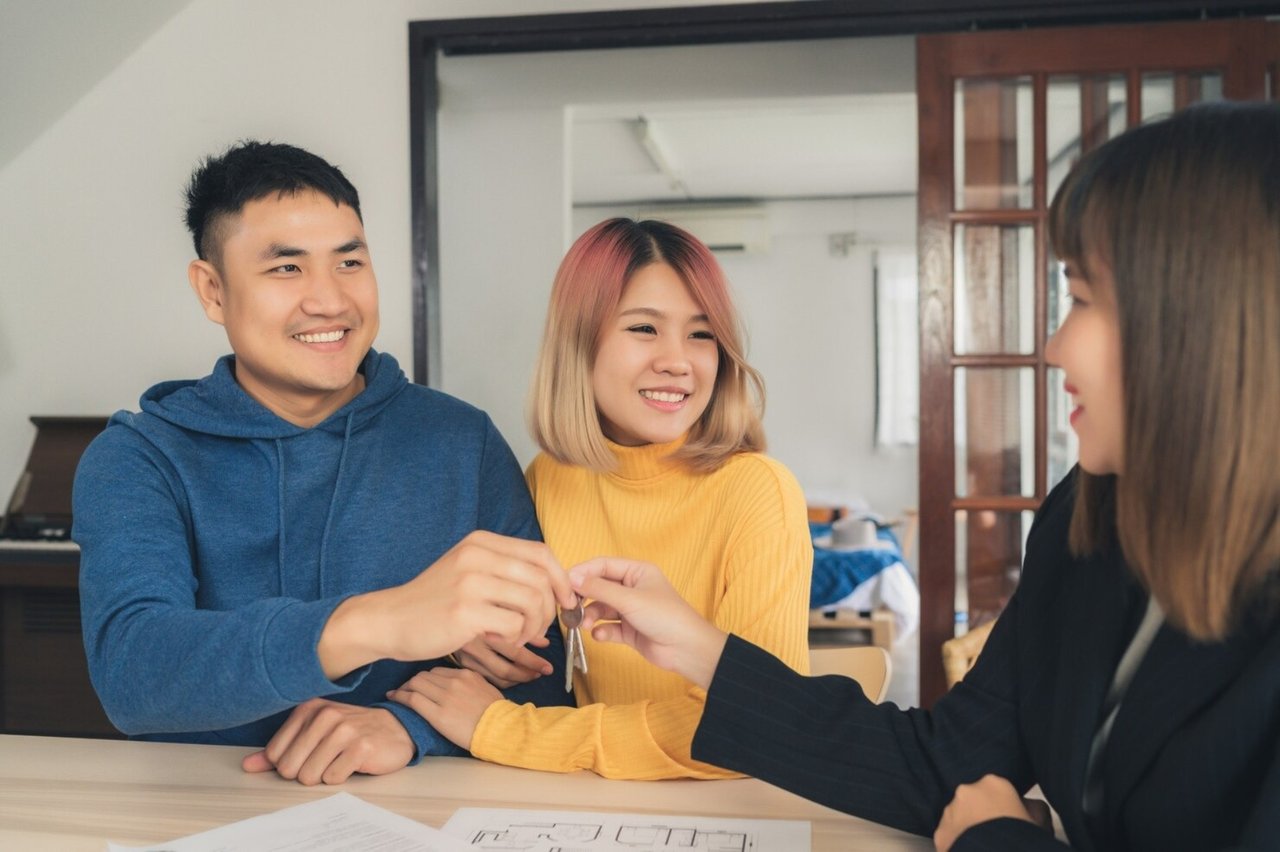 A smiling couple receives house keys from a real estate agent at a table.