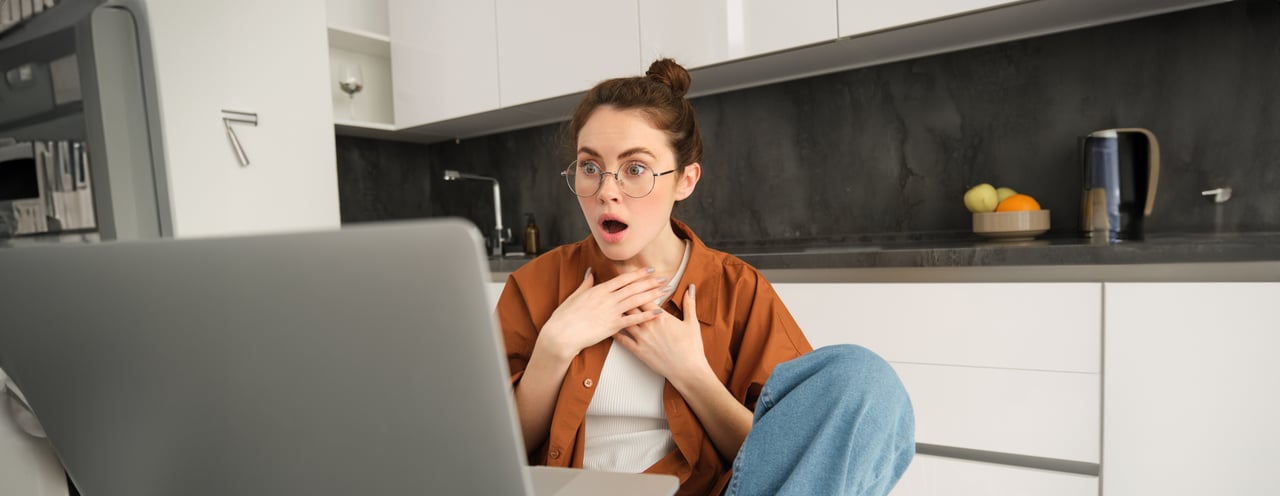 Shocked woman looking at her laptop, reacting to unexpected costs associated with a real estate home purchase.