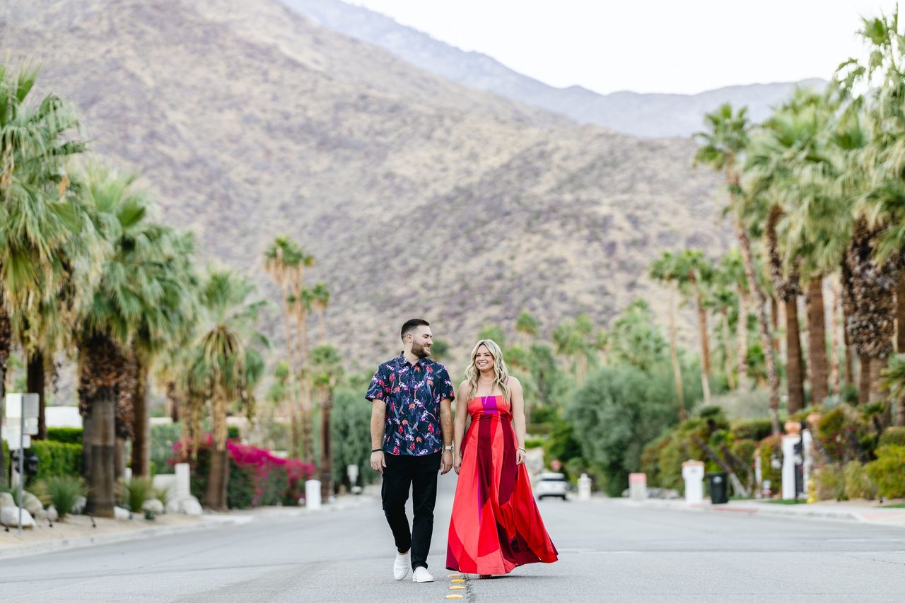 Norman Williams walking a palm-lined Coachella Valley street with desert mountains behind him, Jacqulyn Stanton beside him, lifestyle session.